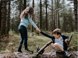 Girl helps her friend across a fallen log in a forest